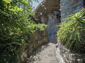 Un étroit sentier de pierres mène à un bâtiment rustique en pierre, dont la façade est ornée d’une horloge.