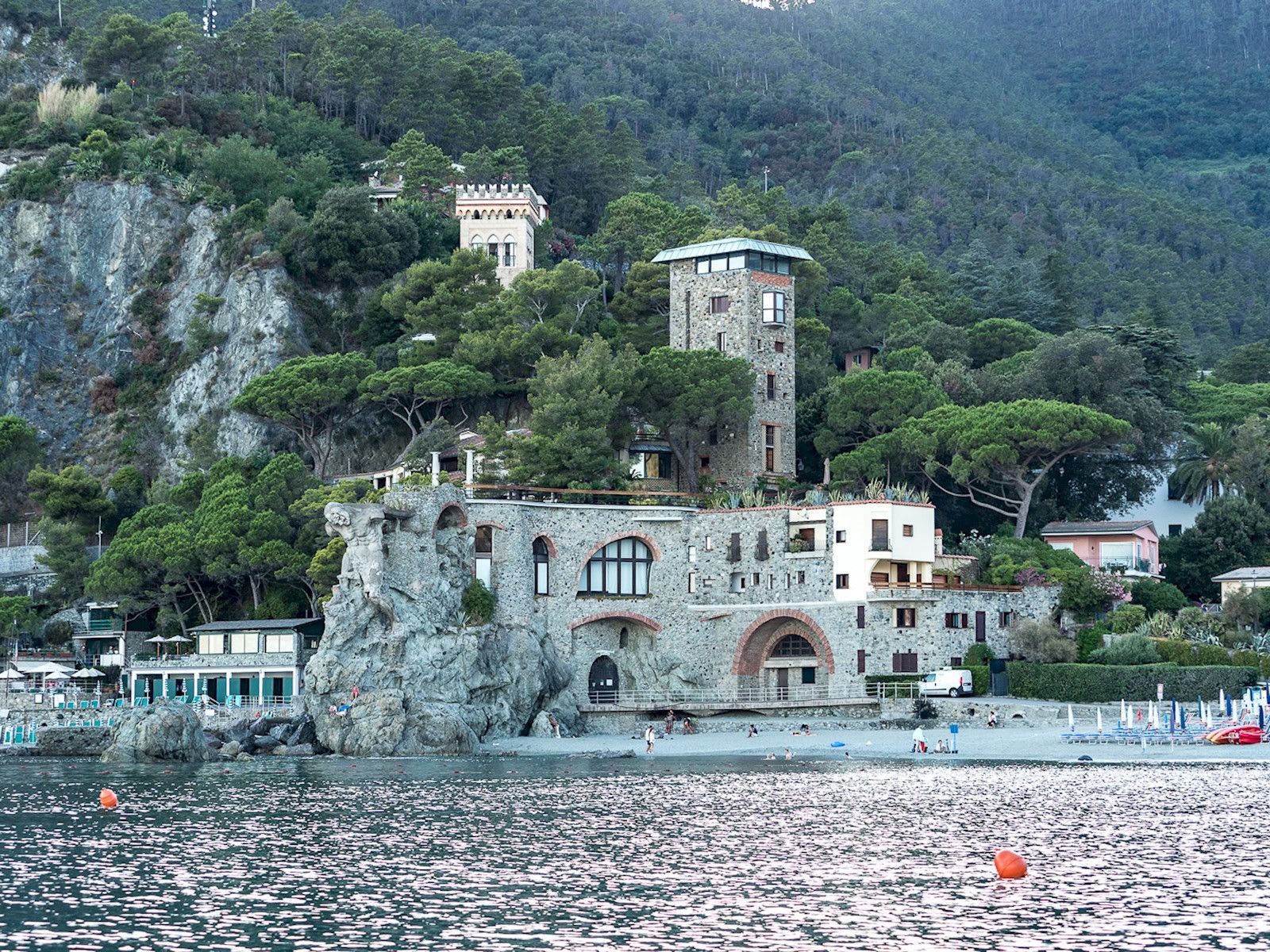 A coastal building with a tower, situated on a rocky cliff with a beach in the foreground.