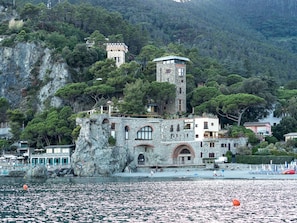 A coastal building with a tower, situated on a rocky cliff with a beach in the foreground.