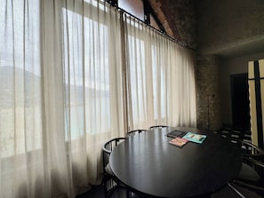 A conference room with a round table, chairs, and a window with sheer curtains.