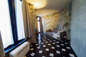 Ein Zimmer mit Schachbrettmuster-Boden, einem Bett, einem kleinen Tisch und einem Fenster mit Vorhängen.