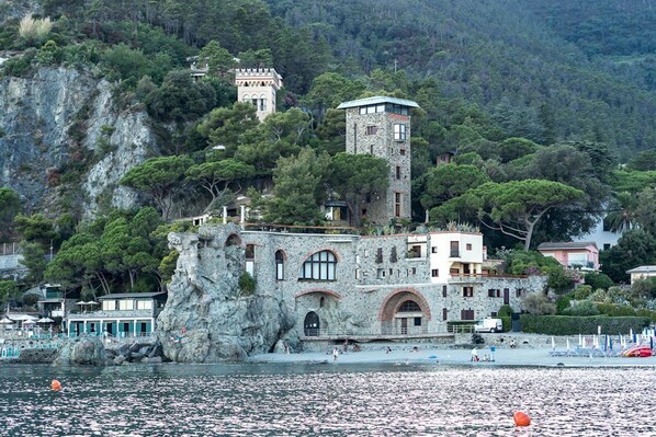 A coastal building with a tower, situated on a cliff with a beach in the foreground.