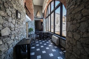 Ein Innenraum mit Steinwänden, einem karierten Boden, einem Tisch mit Stühlen und großen Fenstern mit Blick.