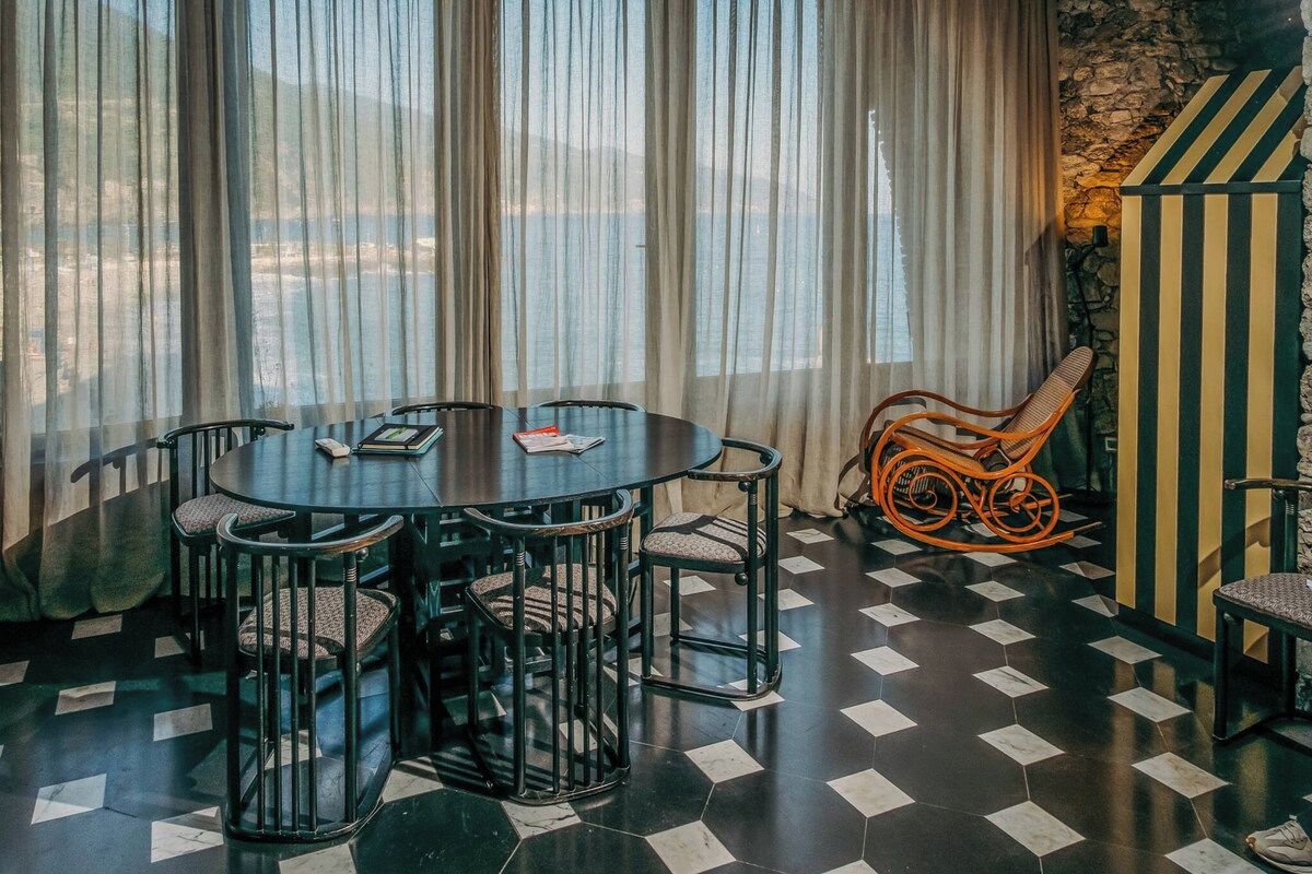 A dining area with a round table and chairs, a wicker chair, and a striped wall.