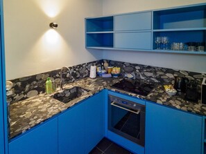 Une cuisine avec des armoires bleues, un comptoir en granit, un four encastré et une étagère murale où sont exposés des verres.