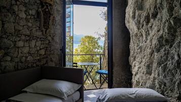 Ein Zimmer mit Steinwand, einem Bett, einem kleinen Tisch und Blick ins Freie.