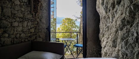 Una habitación con pared de piedra, una cama, una mesita y vistas al exterior.
