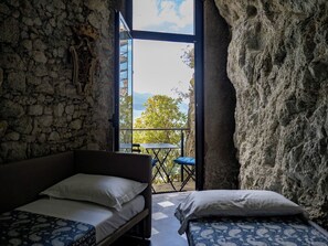 Habitació amb paret de pedra, un llit, taula petita i vistes a l'exterior.