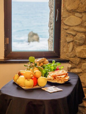 Taula amb fruita, verdura i pa davant d'una finestra amb vista al mar.