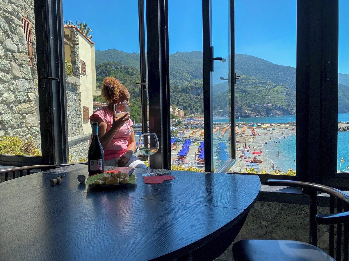 A table with a bottle of wine, a glass, and a plate of food, overlooking a beach with umbrellas and people.