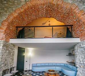 Een loft-stijl kamer met een plafond van baksteen, een blauwe bank en een glazen salontafel.
