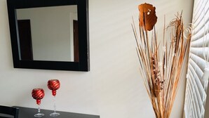 Een moderne kamer met een zwarte console tafel, twee rode decoratieve objecten, een zwarte vaas met gedroogde planten en een grote spiegel aan de muur.