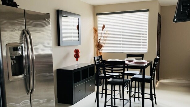 Een moderne keuken met een roestvrijstalen koelkast, een zwart aanrecht en een eethoek met vier stoelen en een tafel.