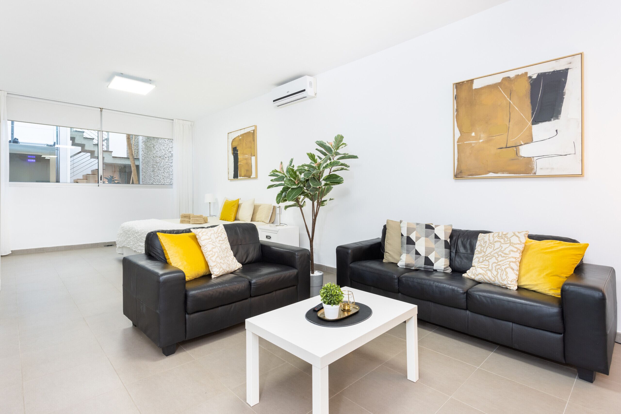 Ein modernes Wohnzimmer mit zwei schwarzen Ledersofas, einem weißen Couchtisch und einem großen abstrakten Gemälde an der Wand.