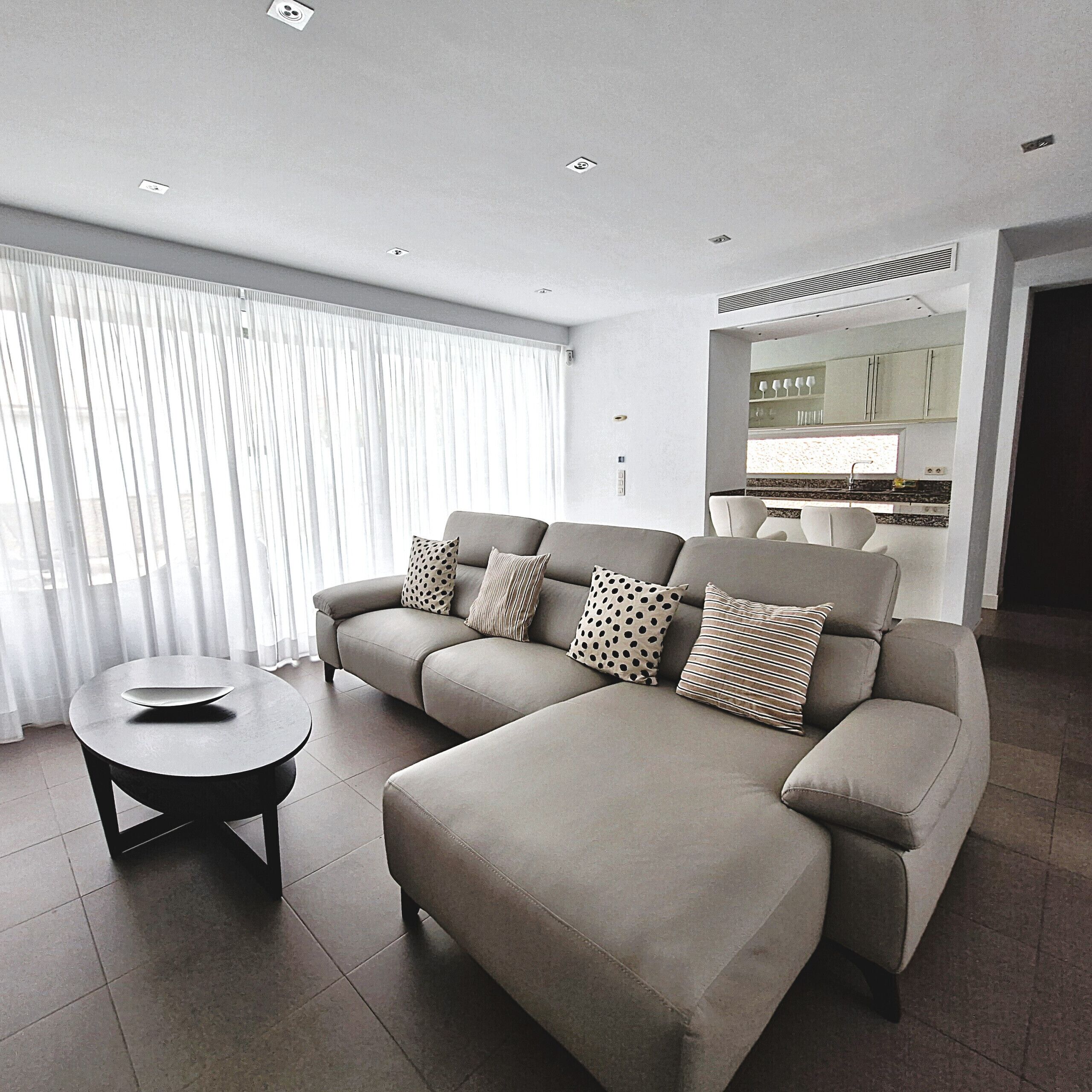 A modern living room with a sectional sofa, a round coffee table, and a kitchen in the background.