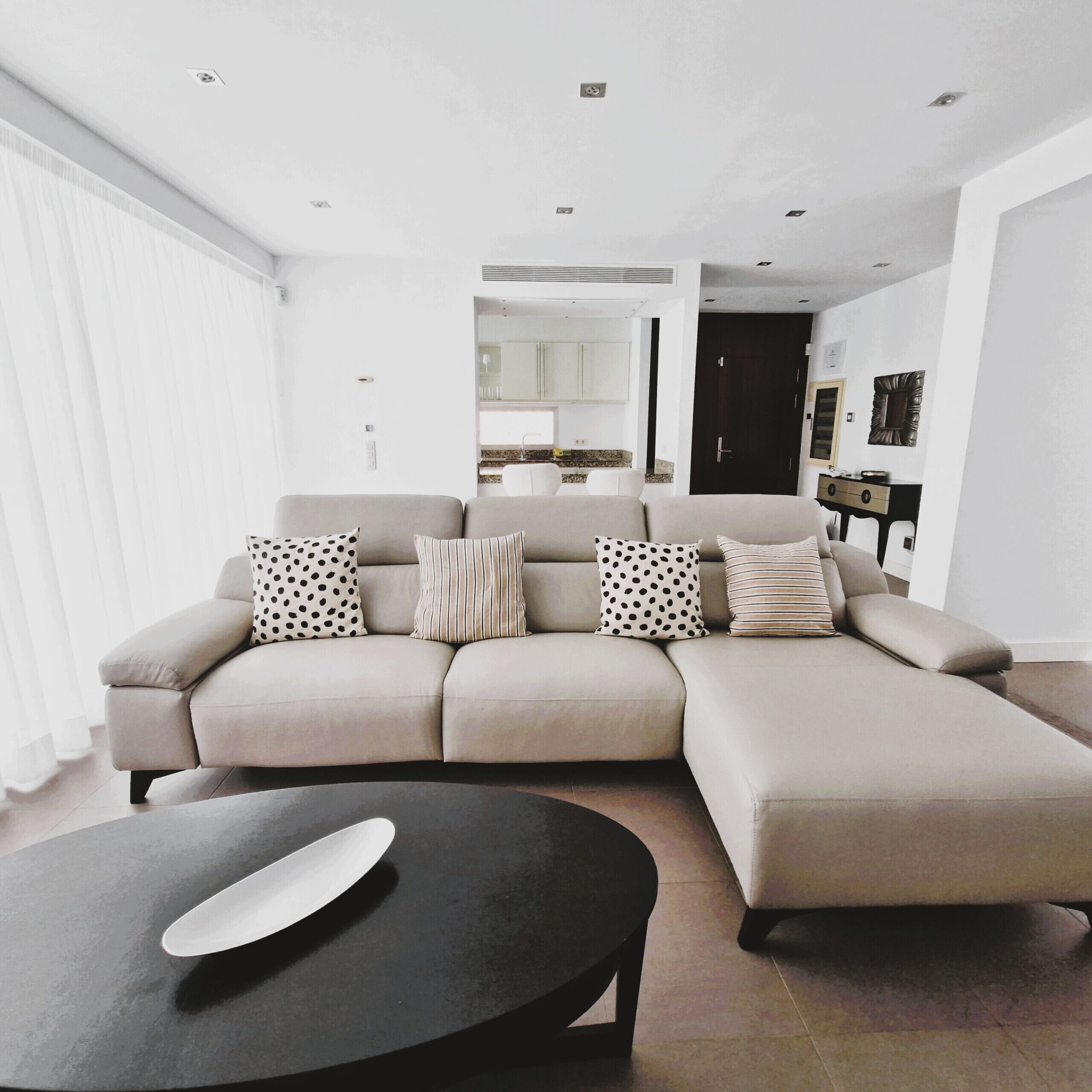 A modern living room with a sectional sofa, a black coffee table, and a kitchen visible in the background.