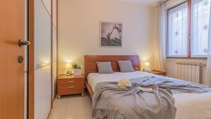 Una camera da letto con un letto in legno, comodini, un tavolino e una finestra con tende, e un quadro appeso al muro.
