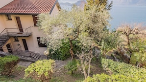 Una casa a due piani con un balcone, immersa nel verde e con vista su un lago e montagne.
