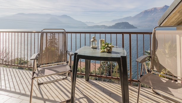 Un balcone con tavolo e sedie che si affaccia su un lago e montagne.