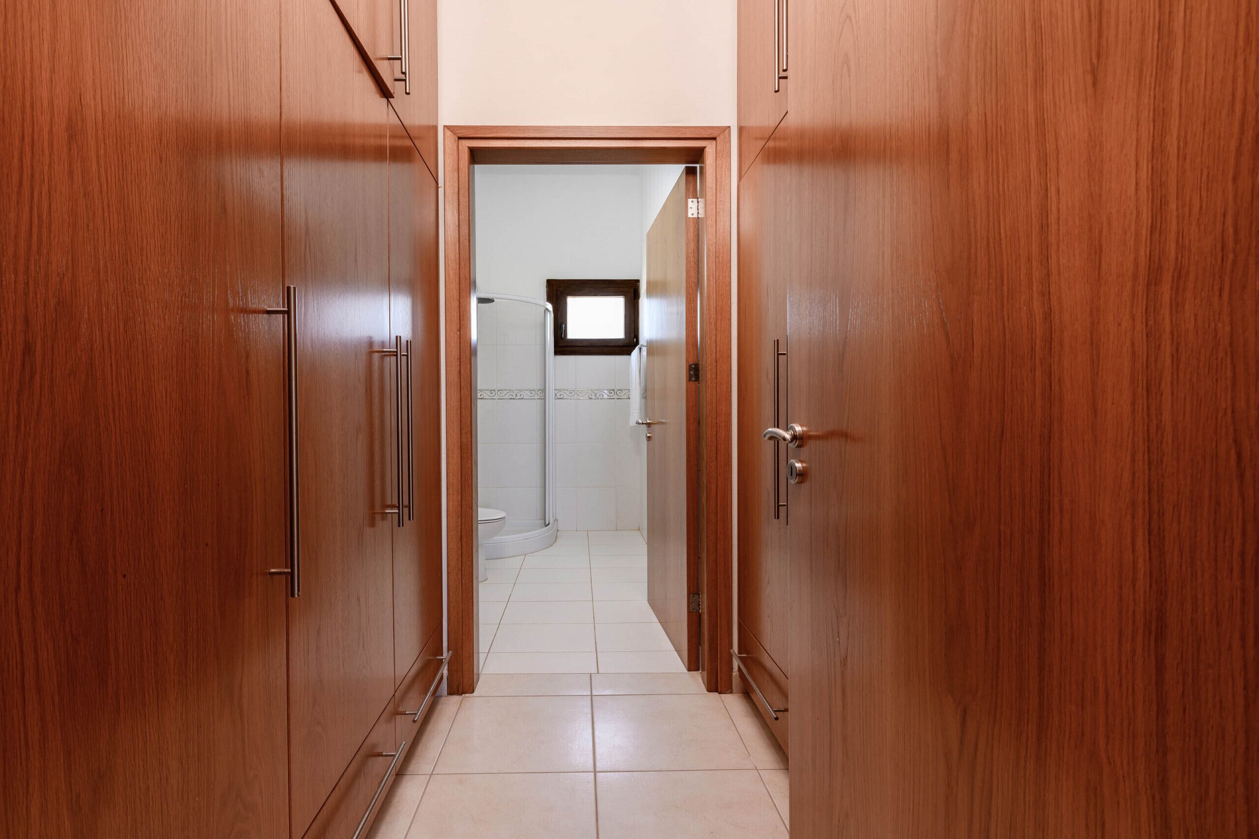 Un couloir avec des portes en bois menant à une salle de bain équipée de toilettes et d’une douche.