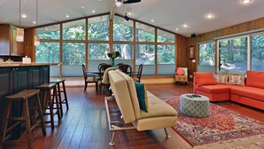 A spacious living area with a large window, a kitchen with bar stools, and a red sofa. - House in the Woods [whole house] (Issaquah)