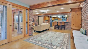 A spacious living area with a large rug, wooden beams, a kitchen in the background, and a sliding glass door. - House in the Woods [whole house] (Issaquah)