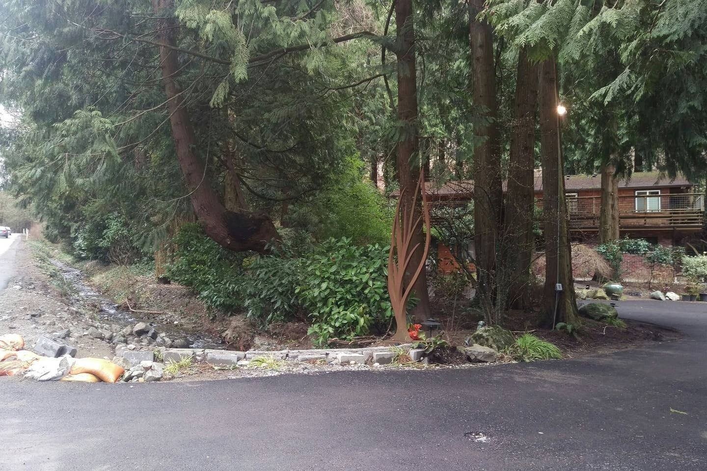 Une route bordée de pierres, bordée d’arbres denses, et un bâtiment doté d’une terrasse en bois.
