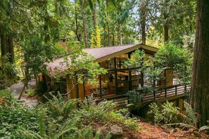 A cabin surrounded by dense forest, with a wooden deck and large windows. - House in the Woods [whole house] (Issaquah)