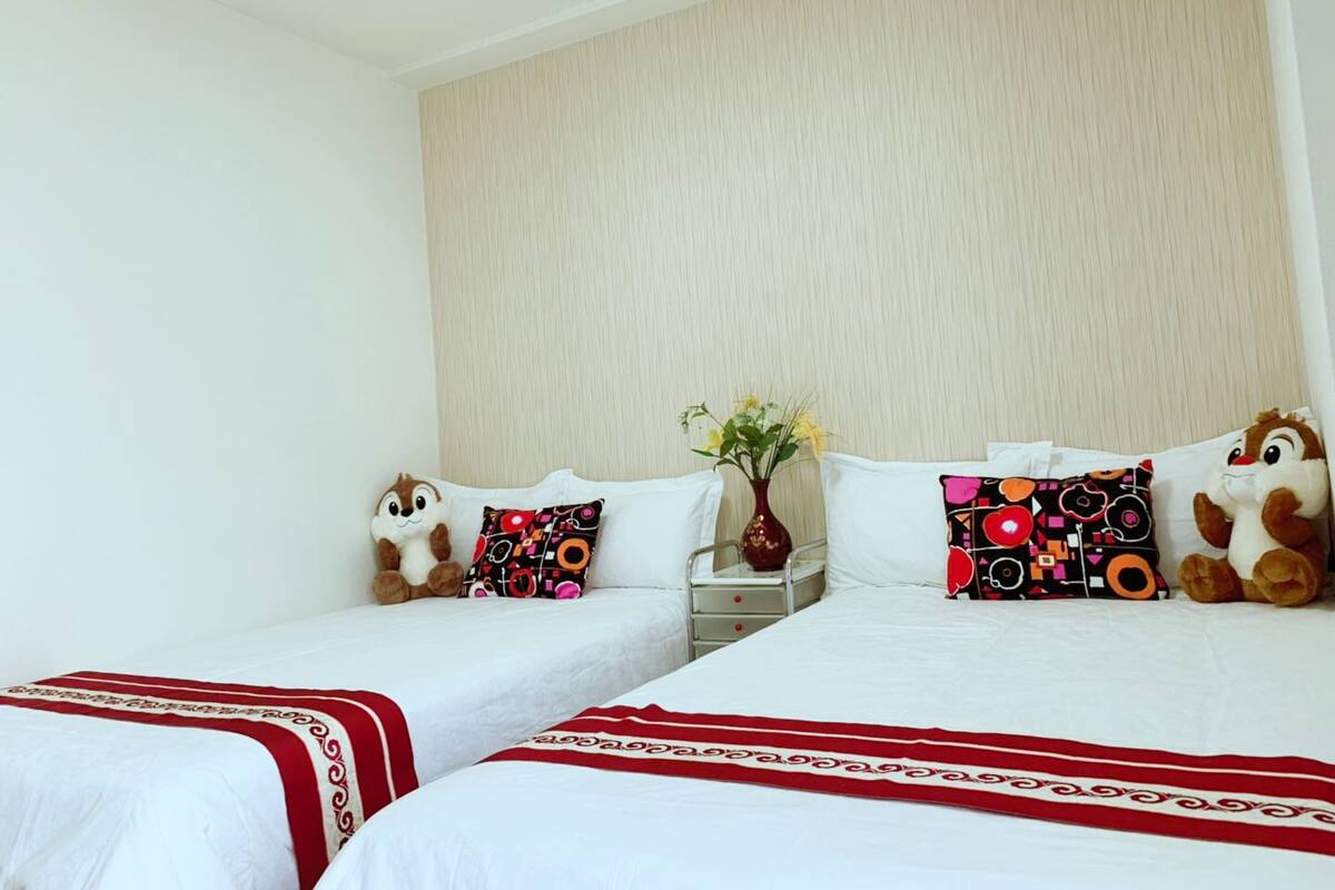 Habitación de hotel con dos camas individuales, una mesita de noche, un jarrón con flores y dos peluches.