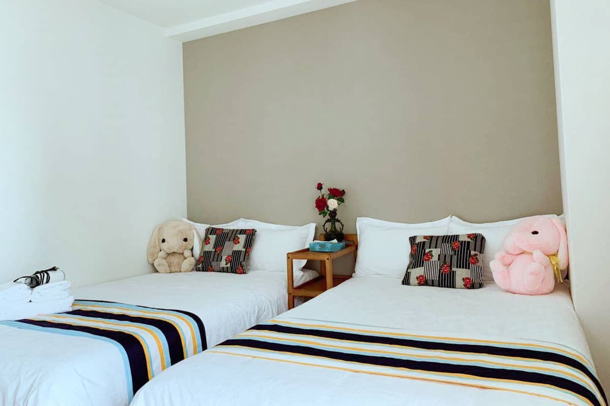 Habitación de hotel con dos camas, ropa de cama a rayas, una mesita de noche con un florero y un osito de peluche en una de las camas.
