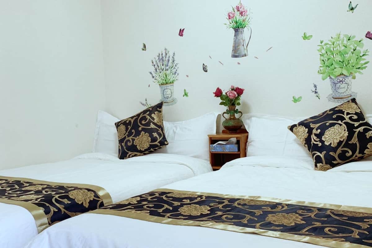 Una cama doble con ropa de cama blanca y almohadas decorativas, una mesita de noche con un florero y un cuadro con flores y mariposas.
