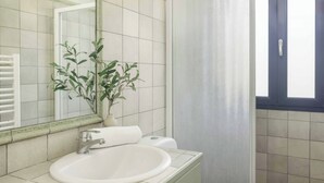 Een badkamer met een wit wastafelmeubel, een spiegel, een plant in pot en een douchegordijn.