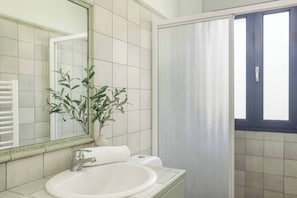 A bathroom with a white sink, a mirror, a potted plant, and a shower curtain. - Villa Nissaki - Two Bedroom Villa, Sleeps 4 (Ionian Islands)