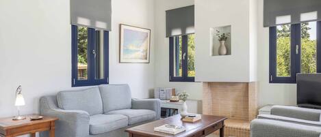 A living room with a sofa, a coffee table, a fireplace, and large windows with shutters.