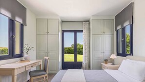 Een slaapkamer met een bureau, stoel, twee bedden, een raam en uitzicht op groen.
