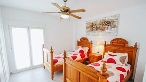 A bedroom with two wooden beds, a ceiling fan, a nightstand with a lamp, and a large window with a view of the outside. - Judith - modern apartment in Moraira (Moraira)