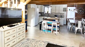 Una cocina acogedora con vigas de madera, una isla central, sillas blancas y una mesa de comedor.