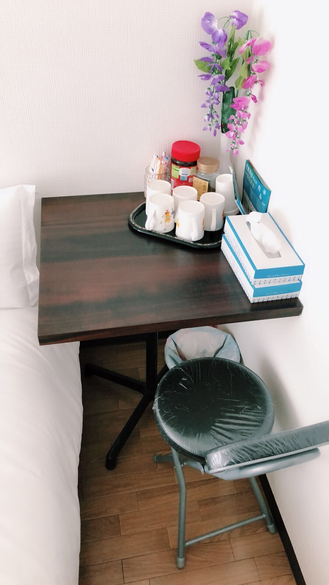 A small dining area with a dark wooden table, white cups, a tissue box, and a chair with a black seat.
