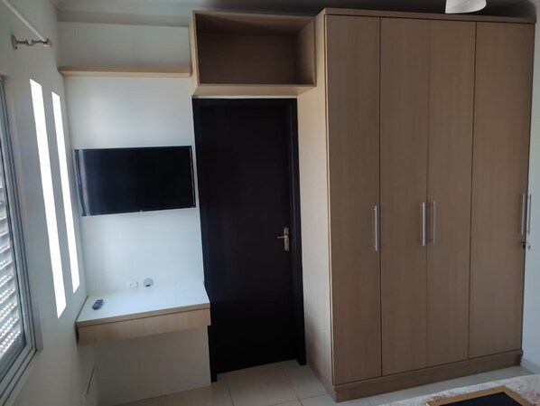A room with a wooden wardrobe, a small desk, and a wall-mounted TV. - Comfortable house in Itapoá, SC, with an 8x4 pool, cable TV, and Wi-Fi. (Itapoá)