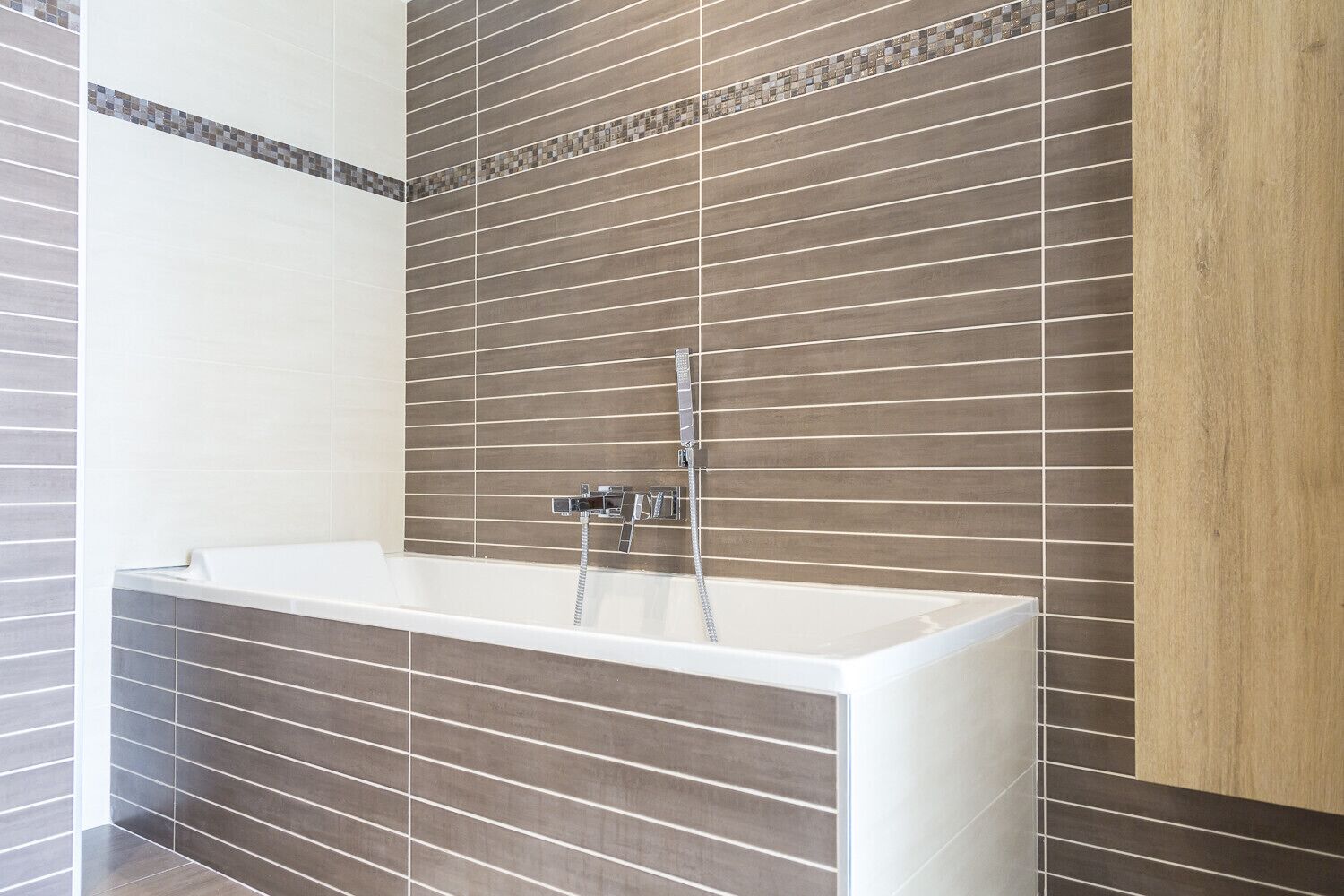 A modern bathroom with a freestanding bathtub, tiled walls, and a wooden panel accent.
