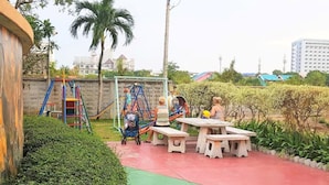 A playground with slides and swings, a picnic table, and a hedge.