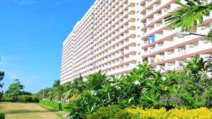 A high-rise hotel with multiple balconies, surrounded by lush greenery and a clear sky.