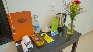 Ett bord med en vattenflaska, en kaffebryggare, en kopp, en vattenkokare, en vas med blommor, en korg med en bok och en skylt.