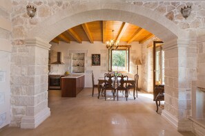 A spacious kitchen with an archway, wooden ceiling beams, and a dining area with a chandelier.