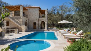 A stone villa with a swimming pool, outdoor seating, and a staircase leading to a balcony. - Villa Melpomeni | in a Forest with Private Pool, Sea View, Gym & Home Cinema (Rethymno)