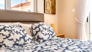 Una cama con ropa de cama estampada, una mesita de noche con lámpara y una ventana con cortinas.