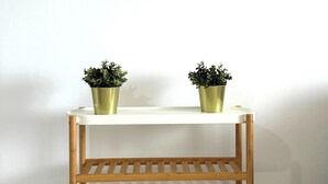 Una mesa de madera con dos plantas en macetas, un reloj de pared redondo y un piso de baldosas.