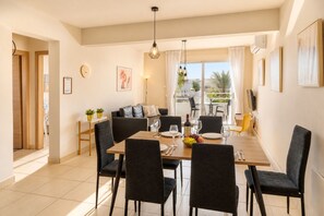 A dining area with a table set for four, chairs, a sofa, and a balcony with a view. - Narcissos 'Nissi Beach' Apartment D12 (Ayia Napa)