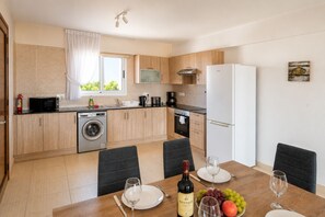 A modern kitchen with a washing machine, a dining table set for two, and a wine bottle. - Narcissos 'Nissi Beach' Apartment D12 (Ayia Napa)