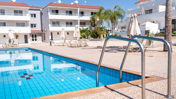 Una piscina con bordes de azulejos, sillas de descanso y sombrillas.